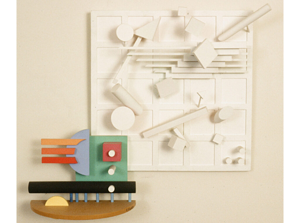 Three-dimensional abstract artwork combining a white grid panel with geometric shapes and colorful wooden elements including red, blue, green, black, yellow, and orange forms, illustrating the artist's early exploration of the third dimension in 1984.